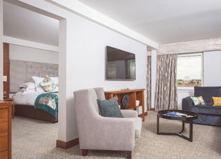 Spacious suite with comfy bed, cosy seating, flat-screen TV, and large window with city view for a relaxing stay.