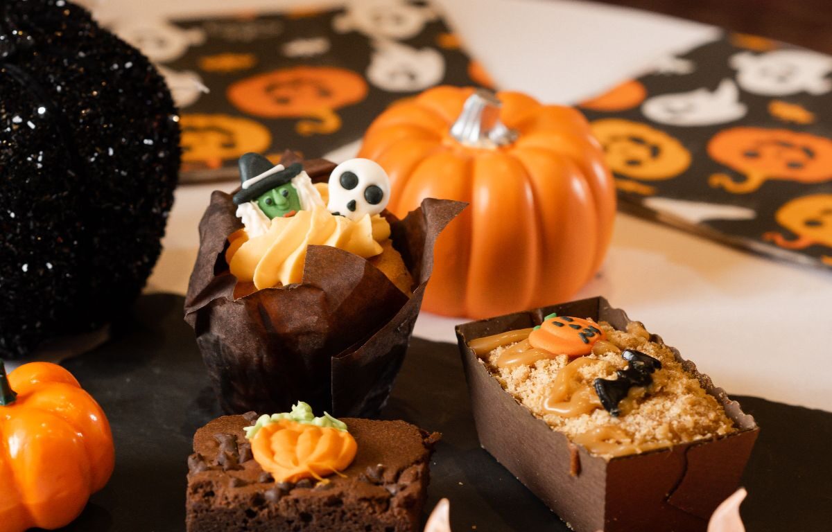 Spooky Halloween-themed desserts on slate with mini pumpkins and flickering candles, creating a cosy and festive atmosphere.